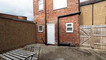 A brick building with a white door, a wooden gate, and a metal table in the foreground.