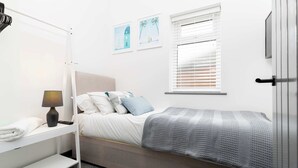 Ein ordentlich eingerichtetes Schlafzimmer mit einem Bett, einem Nachttisch, einer Lampe und einem Fenster mit Jalousien.
