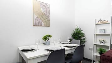 A dining area with a white table set for four, a potted plant, and a decorative wall piece.