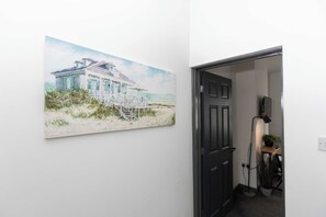 Ein Flur mit einem Gemälde eines Strandhauses, einer schwarzen Tür und einer Lampe.