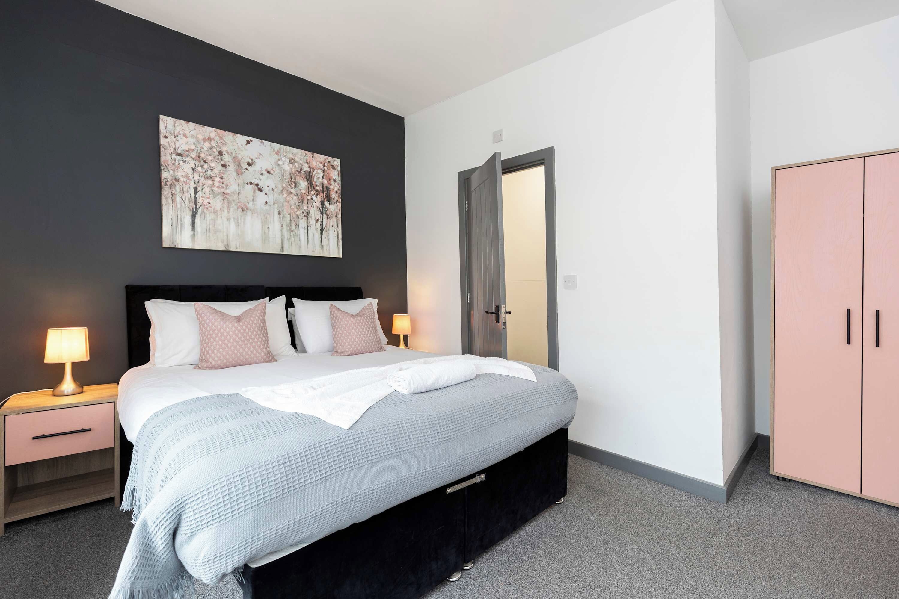 Ein modernes Schlafzimmer mit Bett, Nachttischen, einem Kleiderschrank und einem Bild an der Wand.