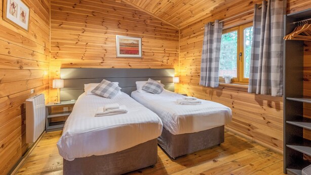 Une chambre rustique en bois avec deux lits, une fenêtre avec des rideaux, un radiateur et un tableau encadré au mur.