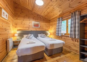 Une chambre rustique en bois avec deux lits, une fenêtre avec des rideaux, un radiateur et un tableau encadré au mur.