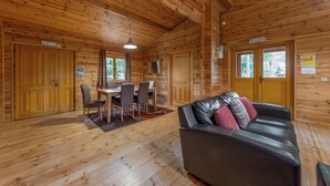 A wooden cabin interior with a dining table, chairs, a leather sofa, and wooden floors. - 3 bedroom accommodation in Ellesmere (Ellesmere)