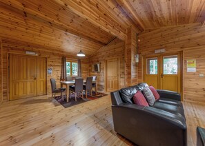 A wooden cabin interior with a dining table, chairs, a leather sofa, and wooden floors. - 3 bedroom accommodation in Ellesmere (Ellesmere)