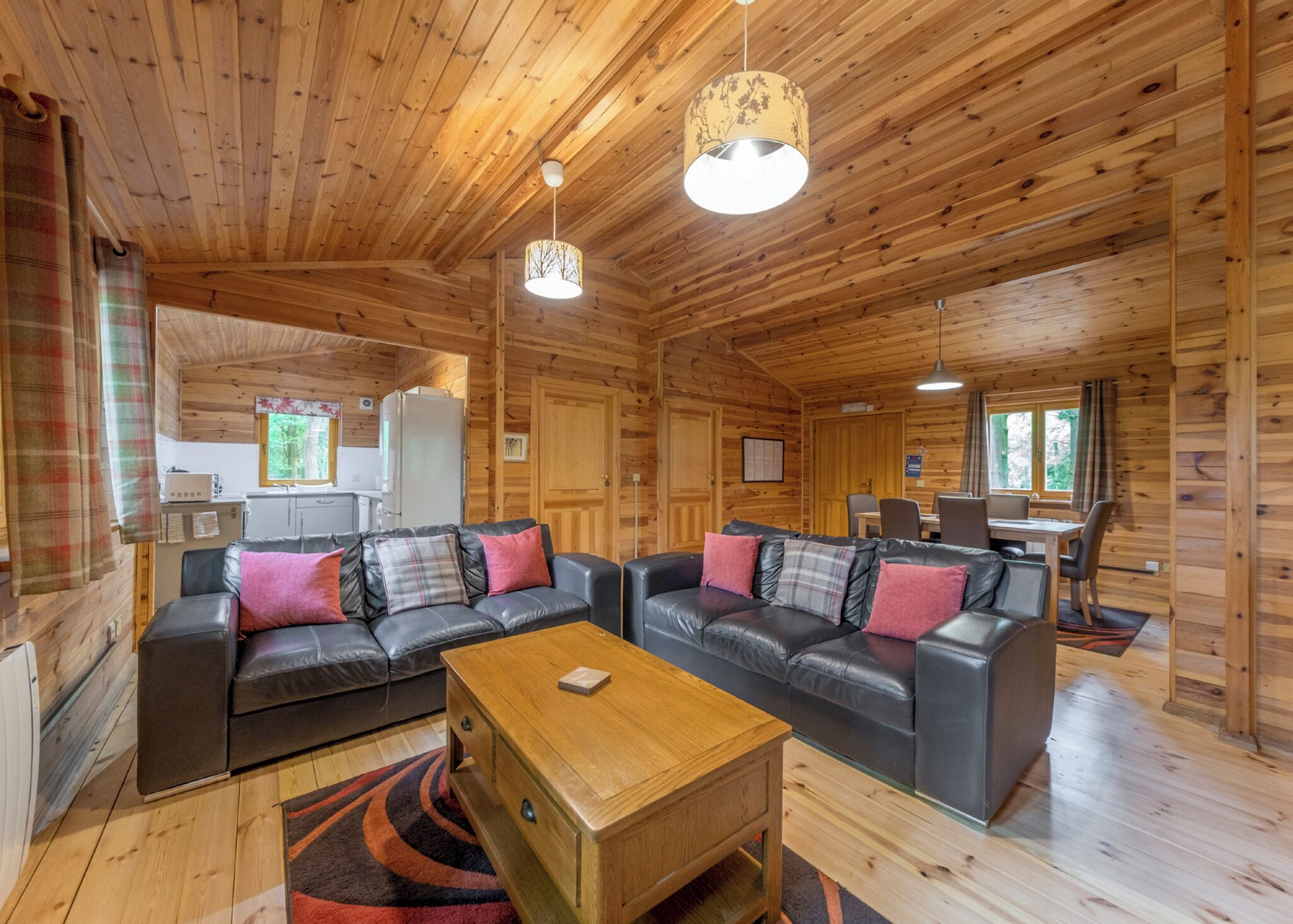 A wooden cabin interior with a living area featuring two sofas, a coffee table, and a dining table with chairs.