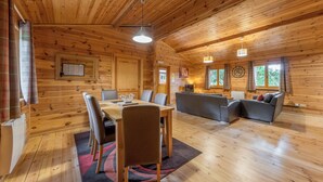 A wooden cabin interior with a dining table, chairs, a sofa, and a television. - 3 bedroom accommodation in Ellesmere (Ellesmere)