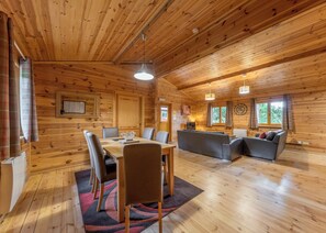 Ein Holzhäuschen im Inneren mit einem Esstisch, Stühlen, einer Couch und einem Fernseher.