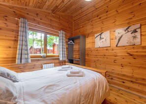 Ein Zimmer mit Holzwänden, einem Bett, einem Fenster mit Vorhängen und zwei Wandbildern.