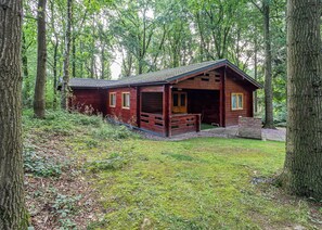 Eine rustikale Holzhütte mit Veranda, umgeben von hohen Bäumen und einer grünen Wiese.