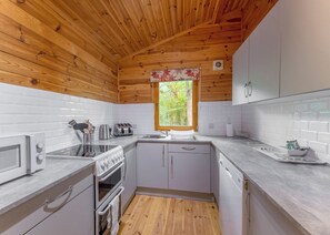 A compact kitchen with wooden ceiling, white tiled walls, a window with a floral curtain, and basic appliances. - 3 bedroom accommodation in Ellesmere (Ellesmere)
