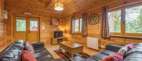 A wooden cabin interior with a sofa, television, and a clock on the wall.