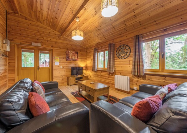 A wooden cabin interior with a sofa, television, and a clock on the wall. - 3 bedroom accommodation in Ellesmere (Ellesmere)