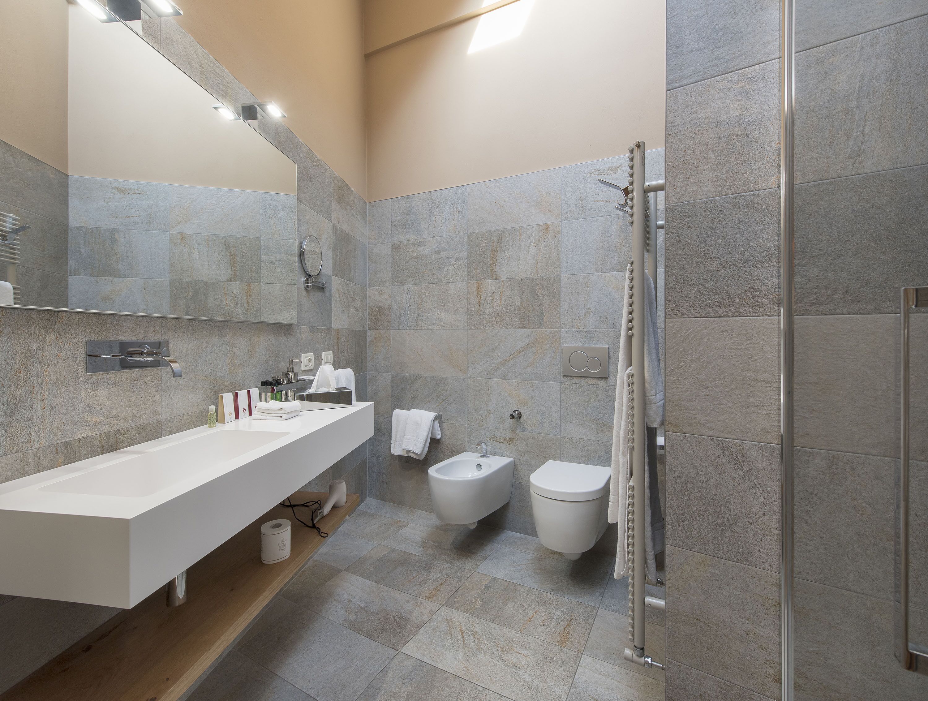 A modern bathroom with a large mirror, a white sink, a toilet, and a shower area.