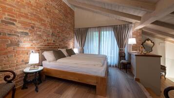 A bedroom with a wooden bed, a brick wall, a small bedside table, a lamp, a chair, and a desk with a mirror.