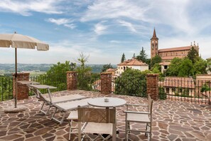 An outdoor patio with a table and chairs, a beige umbrella, and a view of a historic building with a tower. - Sunstar Hotel Piemont (Isola d'Asti)