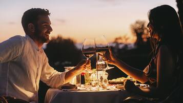Um casal brindando com taças de vinho em uma mesa ao ar livre durante o pôr do sol.