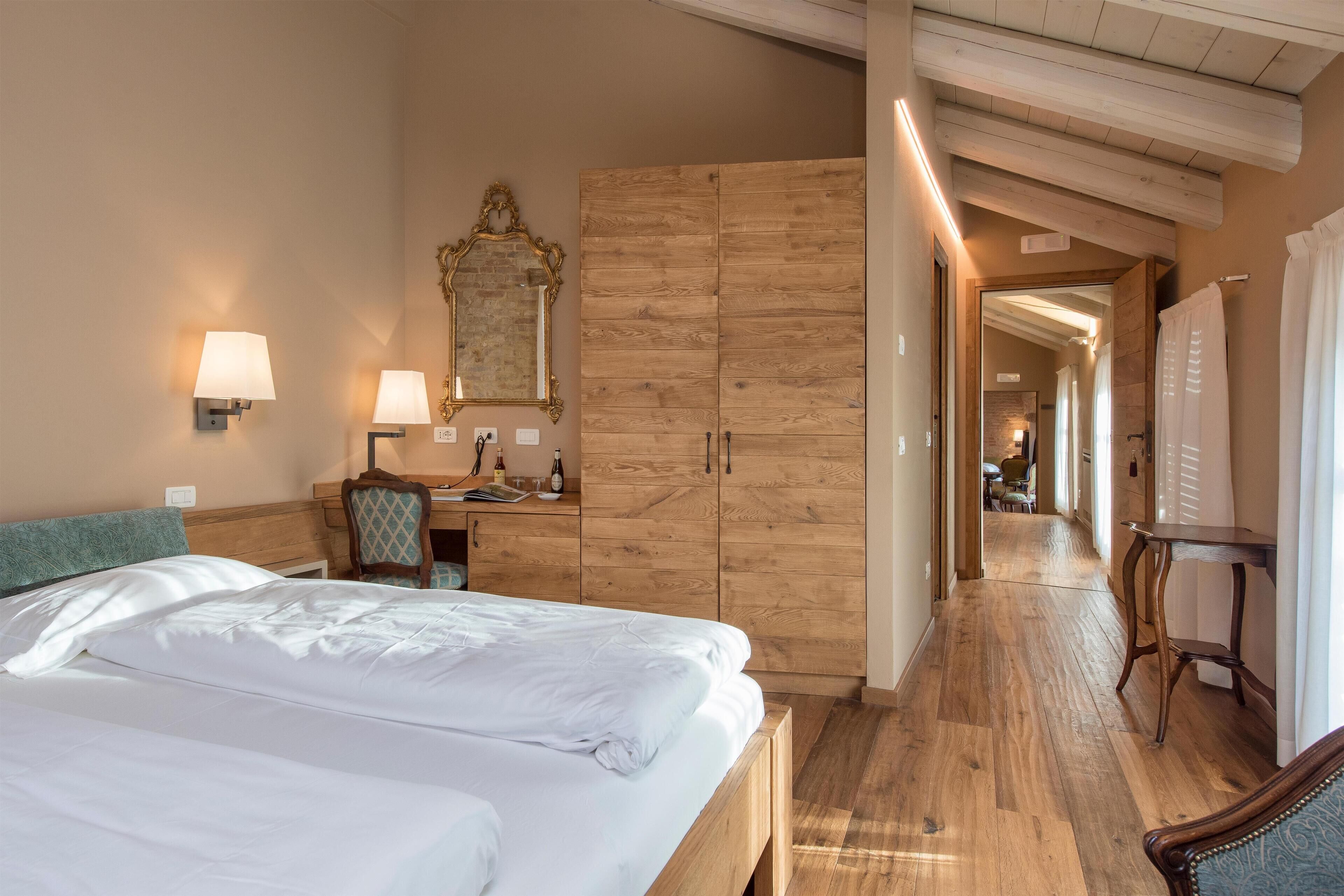 A hotel room with a large bed, wooden wardrobe, desk, and a mirror.