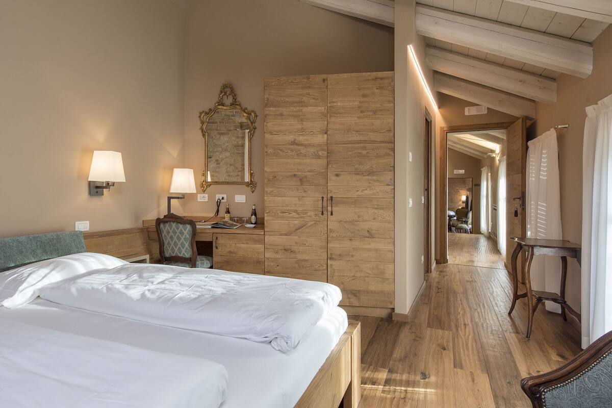 Une chambre d’hôtel avec un grand lit, une armoire en bois, un bureau et un miroir.
