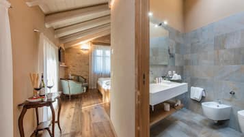 Un baño moderno con un lavamanos grande, bidé y espejo. Hay una mesa de madera con un plato de comida y copas de vino. La habitación tiene una pared de piedra y vigas de madera en el techo.