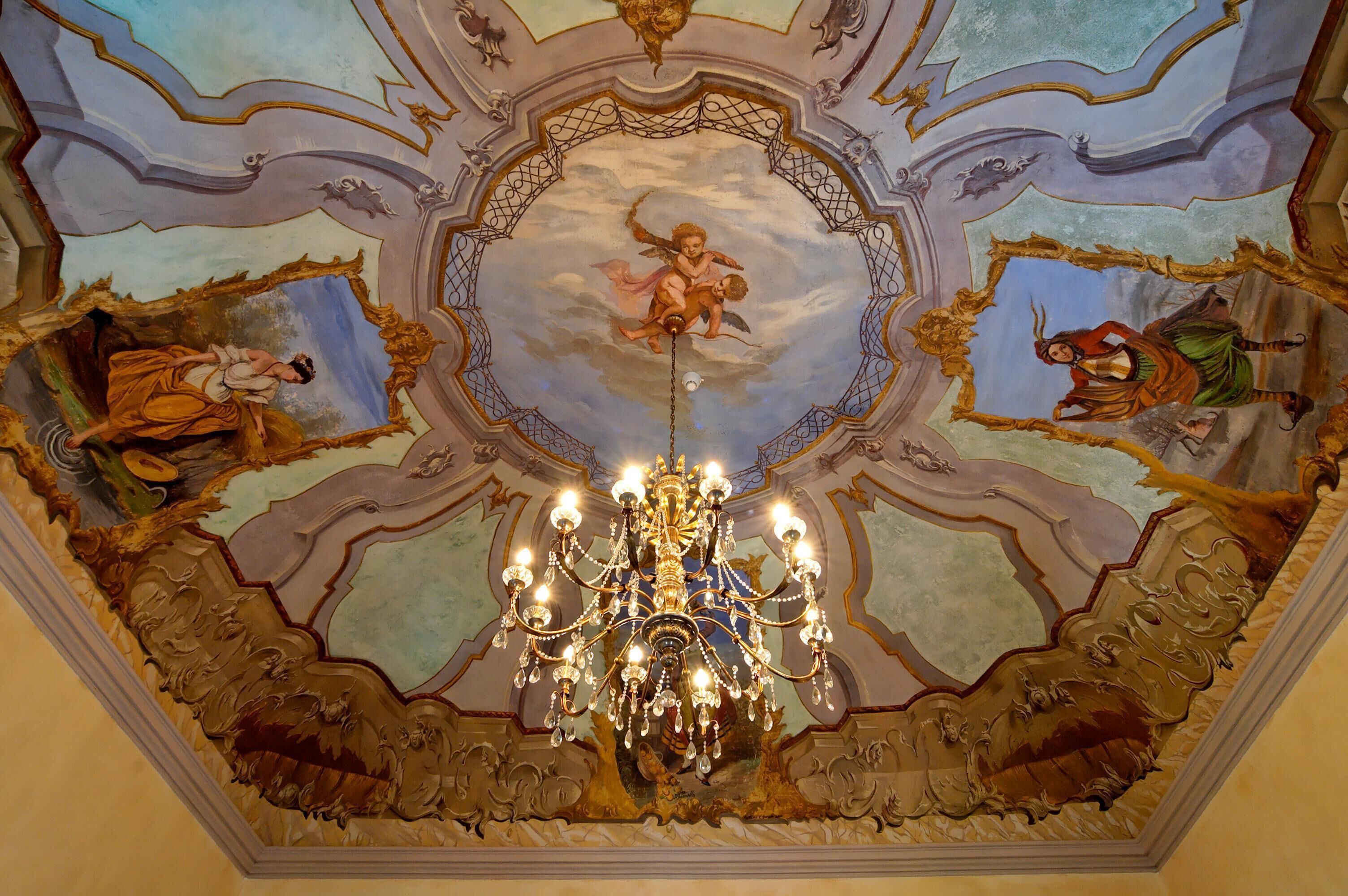A grand chandelier in a room with ornate ceiling artwork and a detailed ceiling design.
