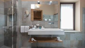 A modern bathroom with a glass shower enclosure, a white sink with a wooden shelf below, and a large mirror above.