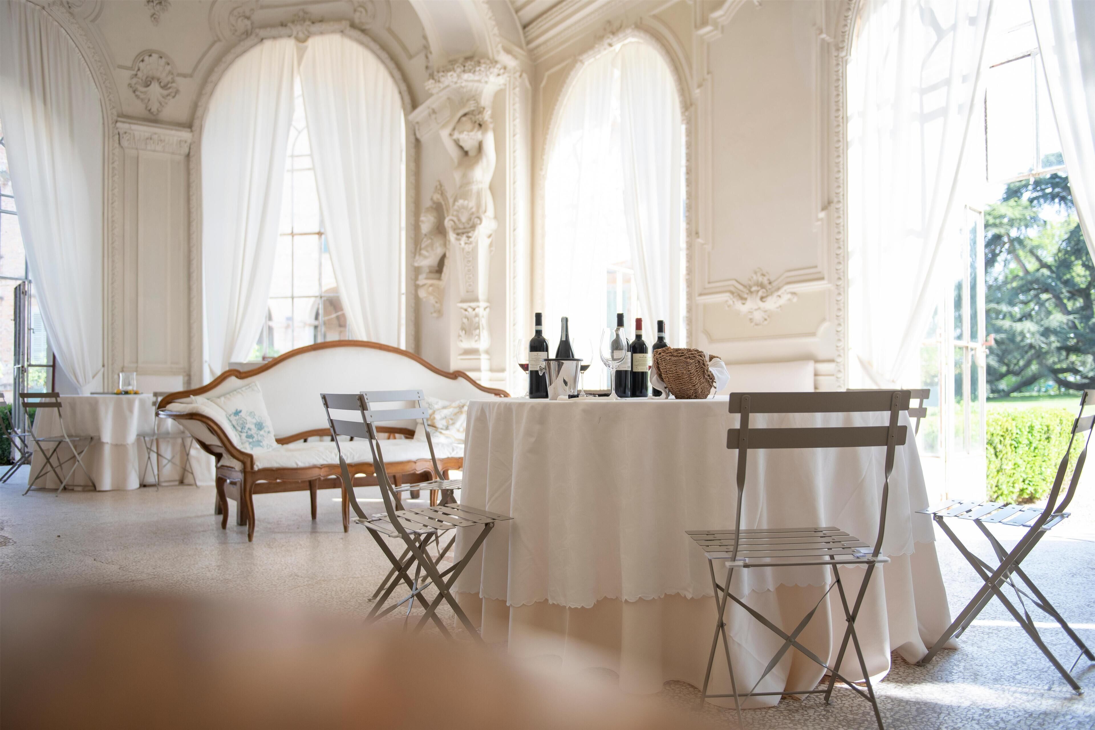 A room with a white table set for a meal, a wooden sofa, and a view of greenery outside.