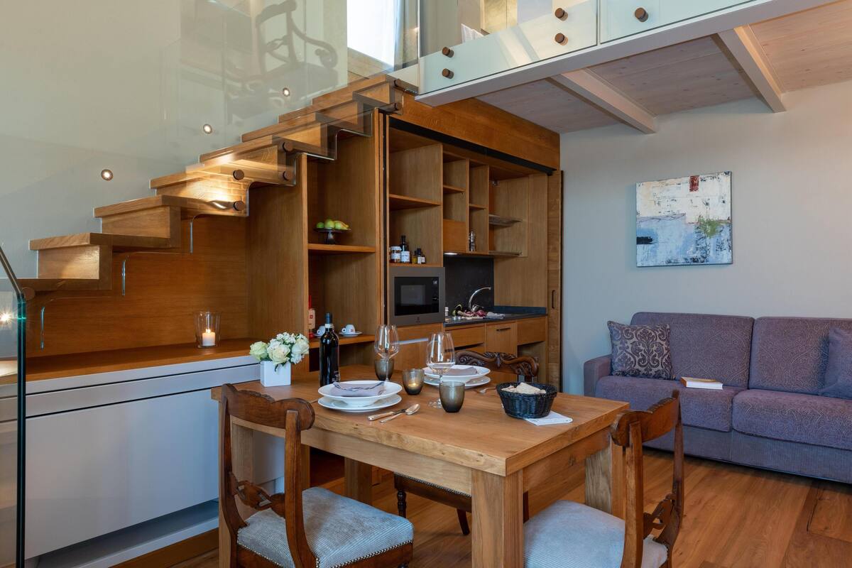 Une cuisine moderne avec des meubles en bois, une table à manger pour quatre personnes et un escalier intégré menant à l’étage supérieur.