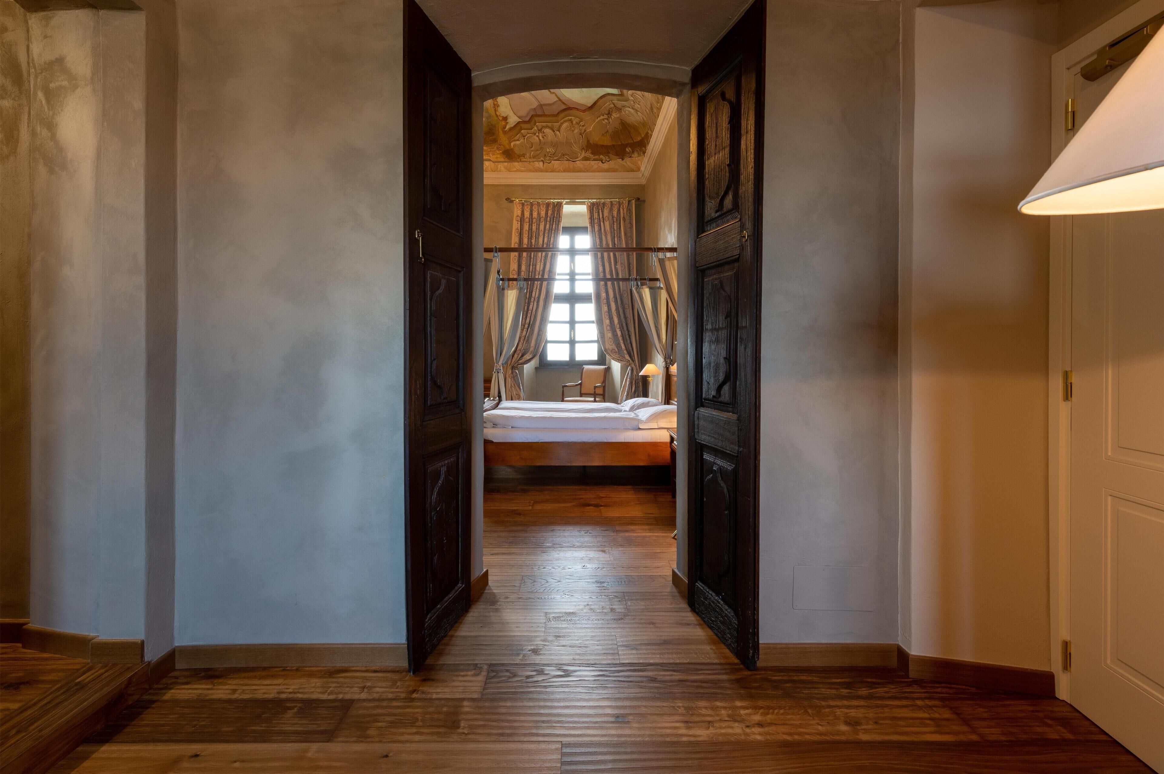 Un pasillo que conduce a un dormitorio con una cama, suelo de madera y un techo con diseño decorativo.