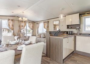 Una cocina moderna con una isla central, comedor con sillas y mesa para cuatro, y vista al exterior.