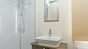Une salle de bain avec une douche à parois de verre, un lavabo blanc avec un meuble-vasque en bois et un miroir au mur.