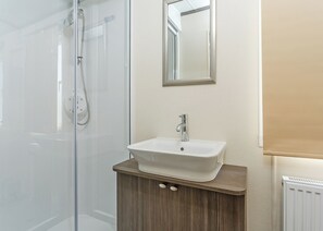 A bathroom with a glass shower enclosure, a white sink with a wooden vanity, and a mirror on the wall.