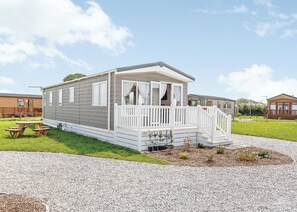 A mobile home with a porch, a small deck, and a picnic table. - Luxurious 14ft-wide holiday home. (Looe)