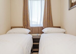 A hotel room with two beds, a window with curtains, and a mirror on the wall. - Luxurious 14ft-wide holiday home. (Looe)