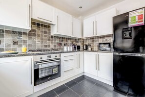 A modern kitchen with white cabinets, a black refrigerator, and a tiled backsplash.