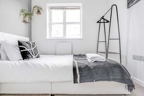 A bedroom with a bed, a window, a radiator, a ladder, and a wall-mounted shelf with plants.