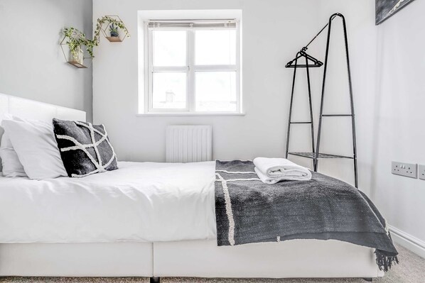 Un dormitorio con cama, ventana, radiador, escalera y estante en la pared con plantas.