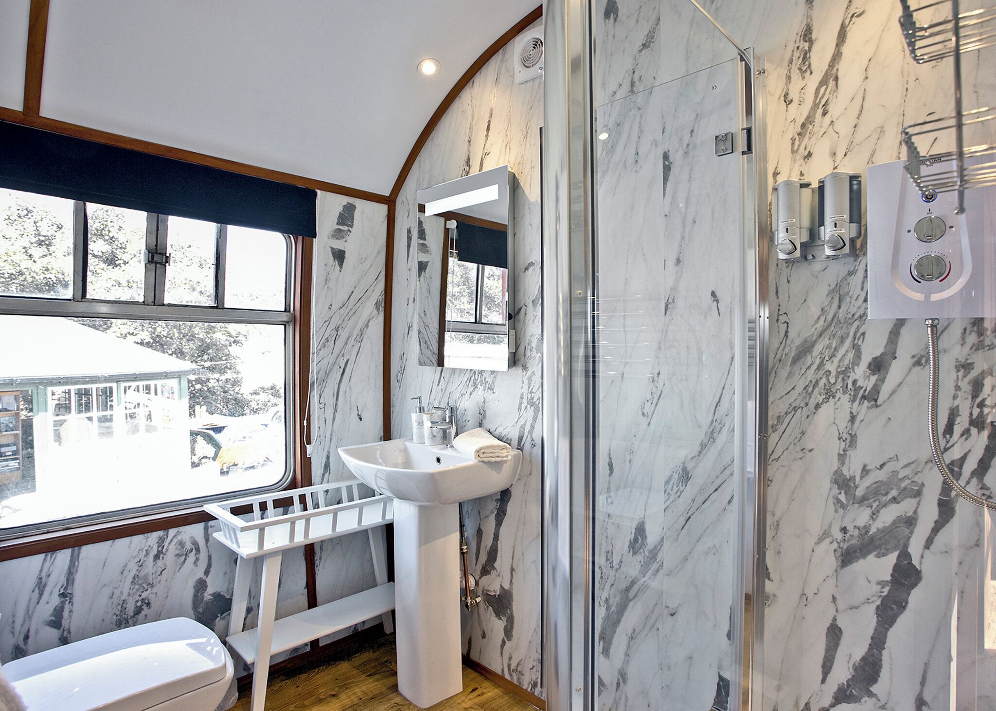 A bathroom with a marble wall, a sink, a mirror, and a shower.
