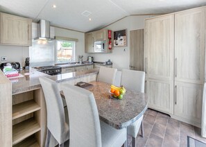 A modern kitchen with a dining area, featuring a granite countertop, stainless steel appliances, and light wood cabinetry.