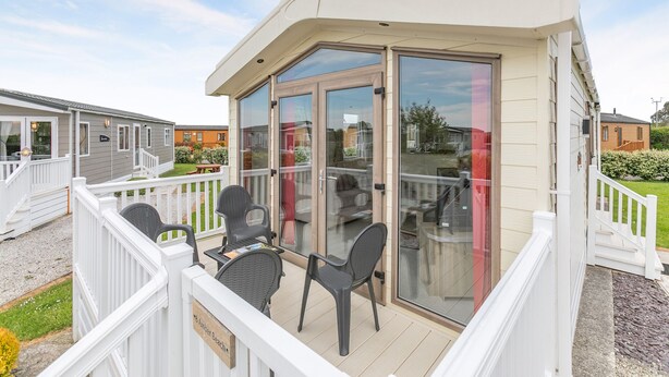 A covered outdoor area with a table and chairs, a glass door, and a white railing.