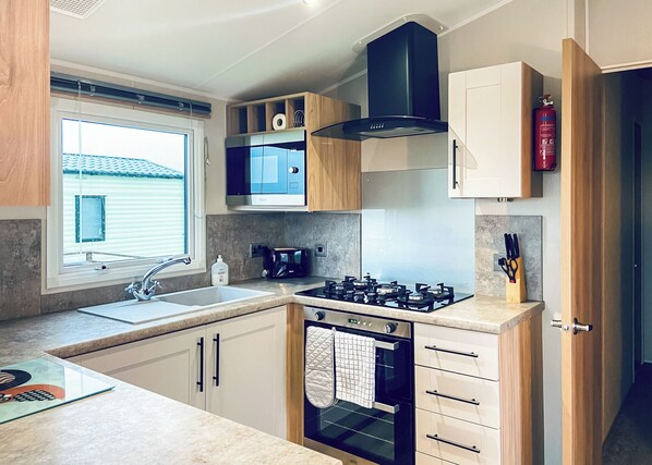 Una cocina moderna con estufa a gas, horno, microondas y una ventana con persianas.