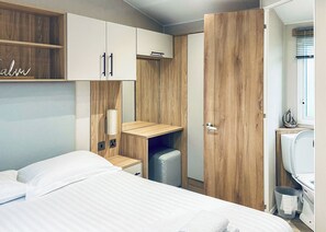 Un dormitorio con cama, armario de madera, escritorio pequeño y baño con inodoro y lavamanos.