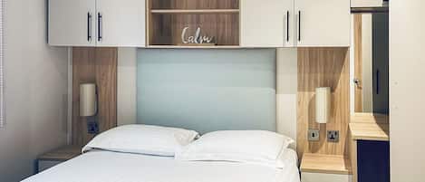 A hotel room with a bed, a bedside table, a nightstand, a wardrobe, and a mirror.