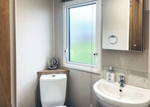 Un baño pequeño con inodoro, ventana, lavamanos y espejo.