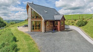 Une cabane en bois avec un toit en pente, de grandes fenêtres en verre et une allée gravillonnée.