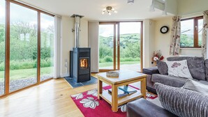 A spacious living room with a wood-burning stove, large sliding glass doors, a sofa, and a coffee table. - Outstanding open plan two storey lodge. (Little London, Nr Llandinam)