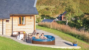 Une cabane en bois dotée d’un bain à remous, d’un espace extérieur aménagé et offrant une vue sur une colline.
