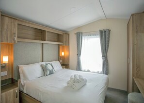 A hotel room with a bed, wooden headboard, bedside lamps, a window with curtains, and a towel on the bed.