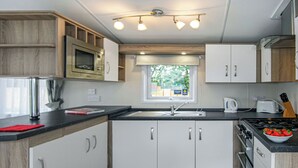 A modern kitchen with white cabinets, a black countertop, a window, and a stove. - 2 bedroom accommodation in Cowden, Nr Hornsea (Cowden, Nr Hornsea)