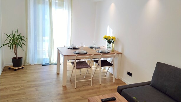 A modern living room with a dining area, a grey sofa, a wooden coffee table, and a potted plant. - FeWo Wildflecken - Holiday apartment Rhön new building 2021 (Wildflecken)